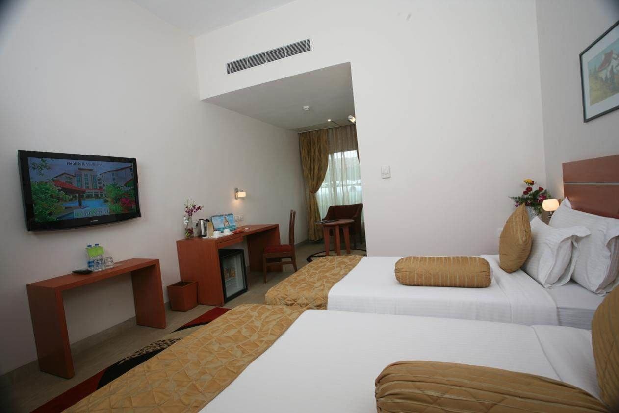 A hotel room with two beds, a desk, a chair, a television, and a small table.