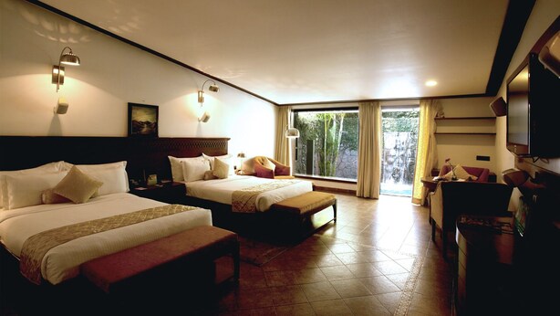 A hotel room with two beds, a desk, a chair, a TV, and a large window with curtains. - Celestia Suites at Leonia (Shamirpet)