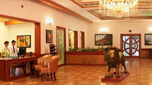 A hotel lobby with a reception desk, a help desk, a receptionist, and a lion statue. - Celestia Suites at Leonia (Shamirpet)