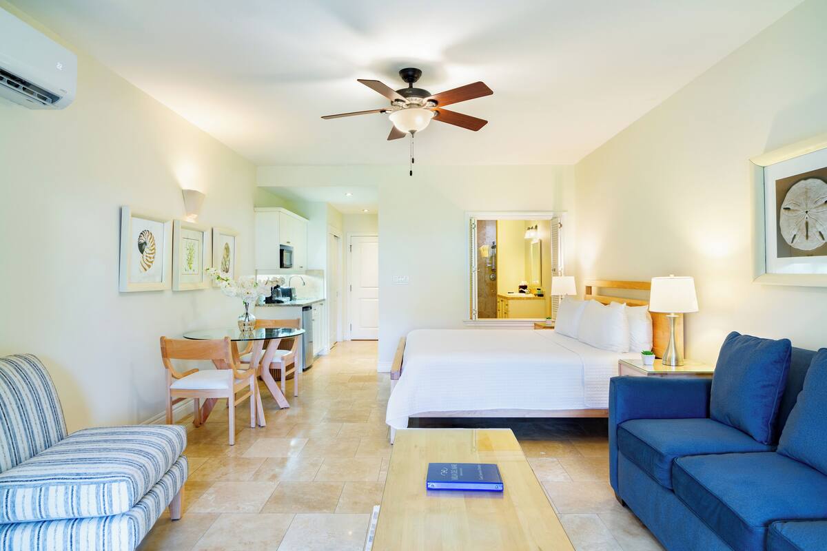 A hotel room with a bed, a blue sofa, a wooden coffee table, a desk with a chair, and a ceiling fan.