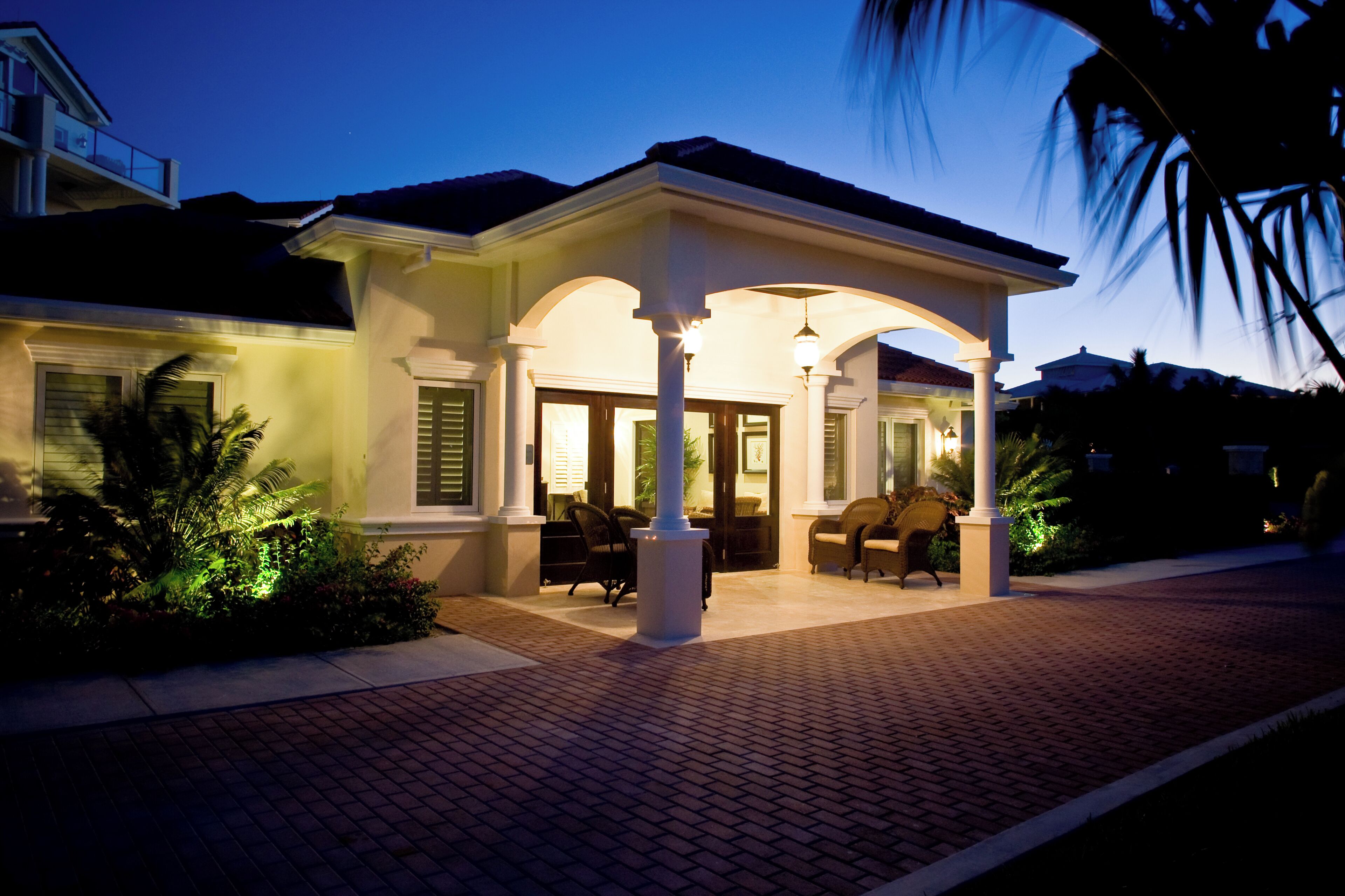 A well-lit house with a covered porch, a brick pathway, and a palm tree.