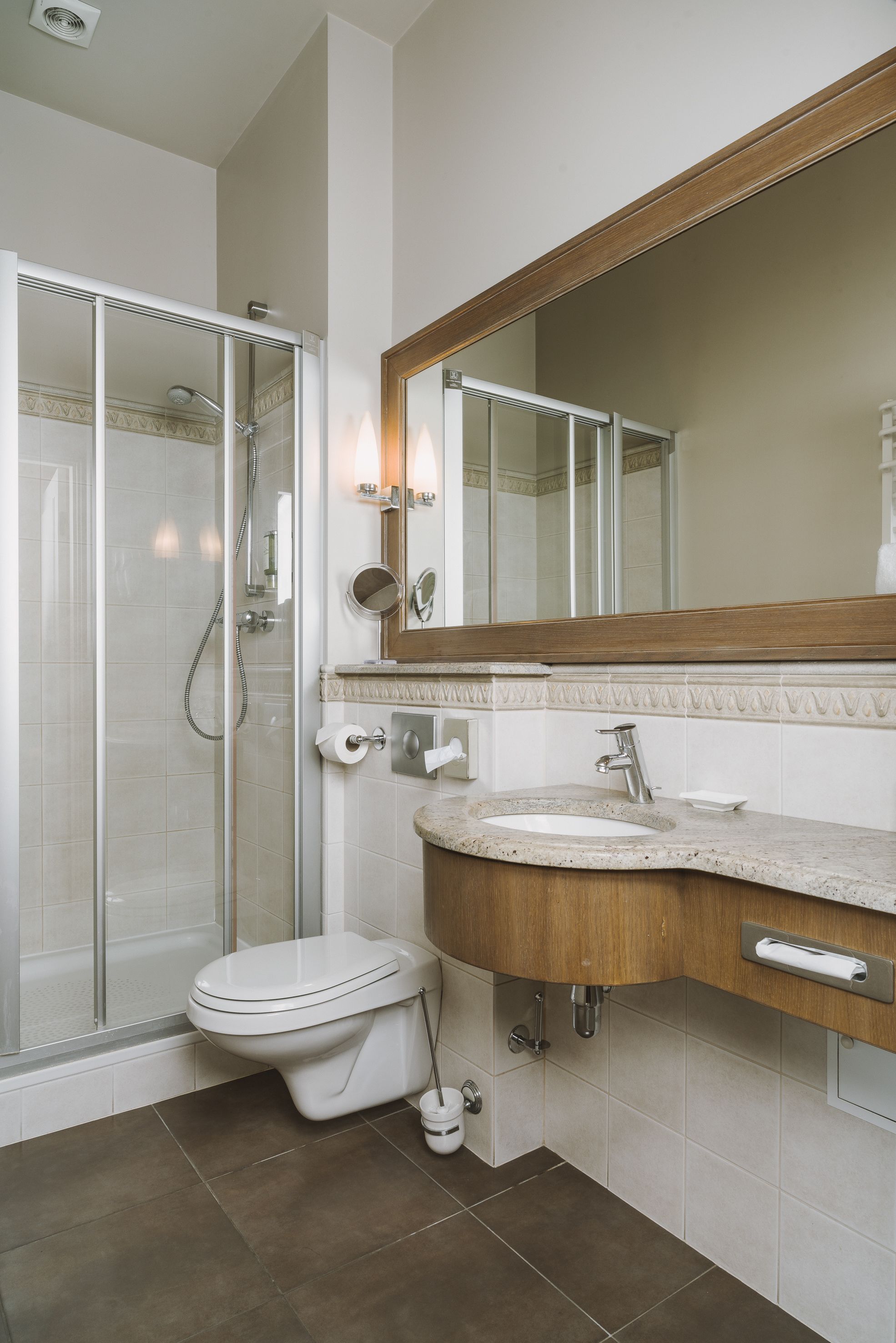 A modern bathroom with a glass-enclosed shower, a wooden vanity, a large mirror, and a toilet.