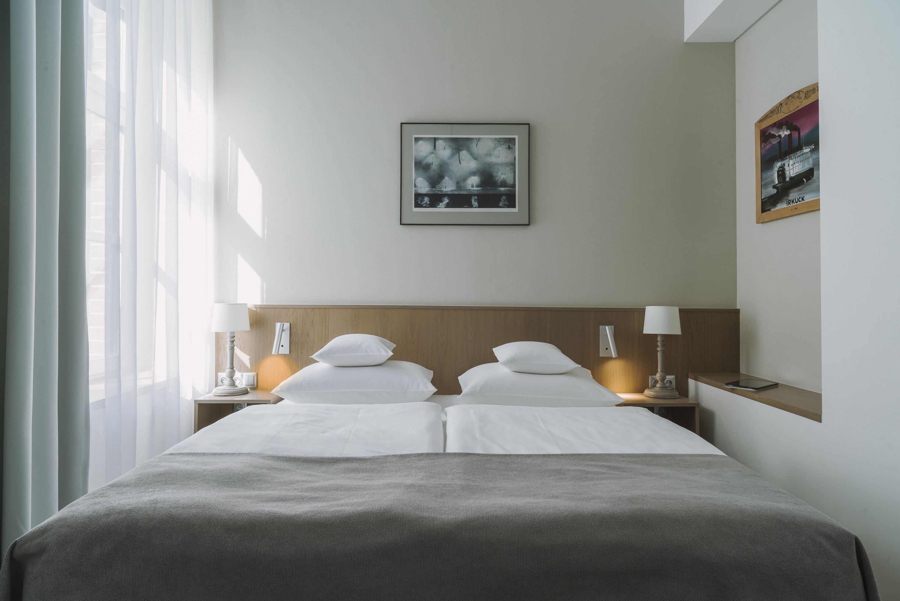 A hotel room with a large bed, two bedside tables with lamps, a framed picture on the wall, and a window with sheer curtains.
