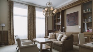 A living room with a sofa, armchairs, a coffee table, and a chandelier. There is a bookshelf with books and a painting on the wall. - Art Hotel (Wroclaw)