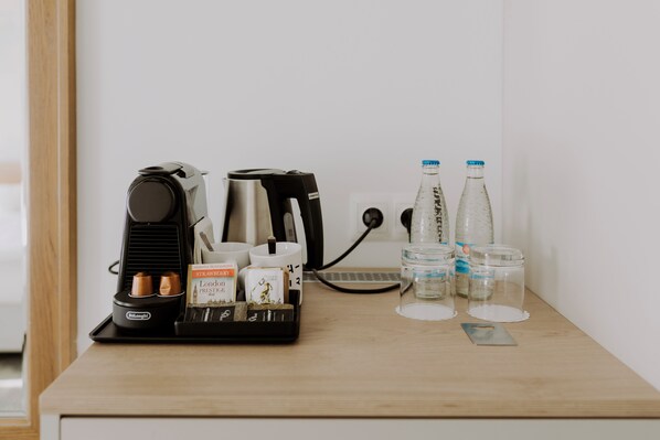 A coffee station with a coffee maker, cups, and a tray with coffee pods and a coffee bag.
