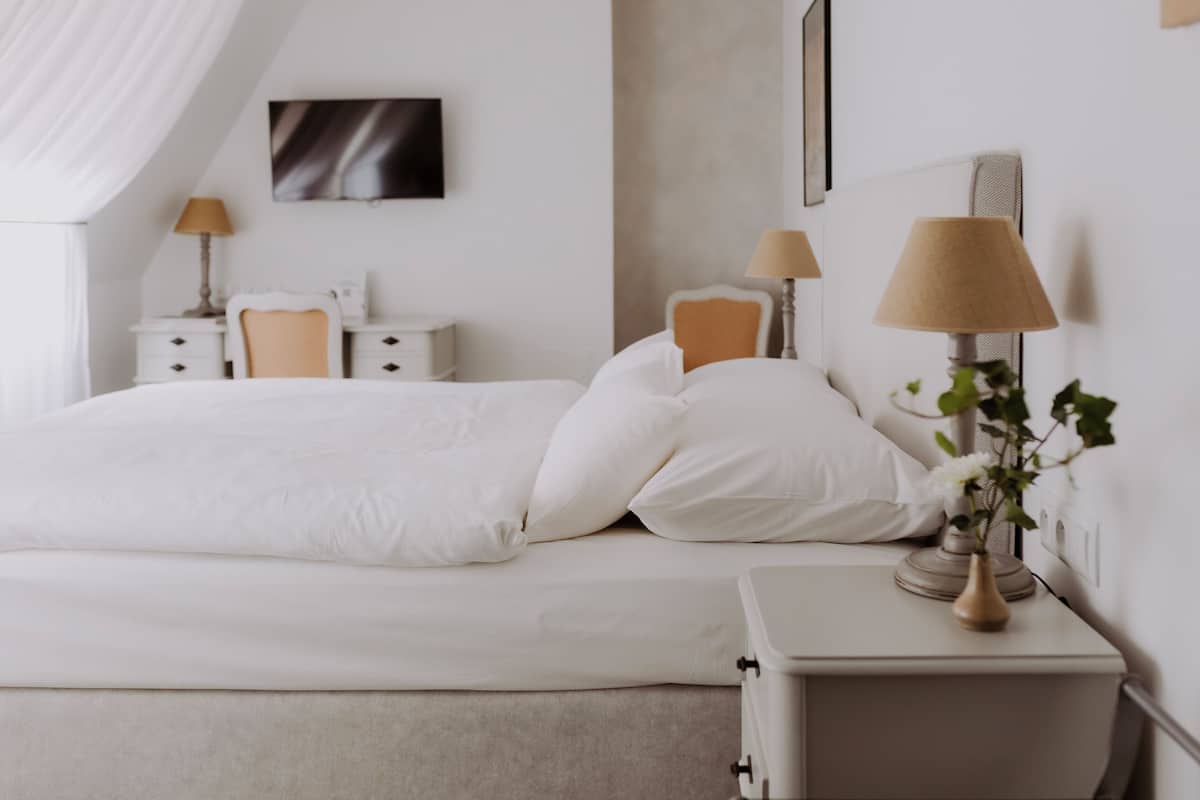 Un dormitorio ordenado con cama, mesitas de noche, lámparas y un florero con flores.