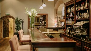 A bar area with a long counter, several cushioned bar stools, a large vase with flowers, and shelves stocked with bottles. - Art Hotel (Wroclaw)