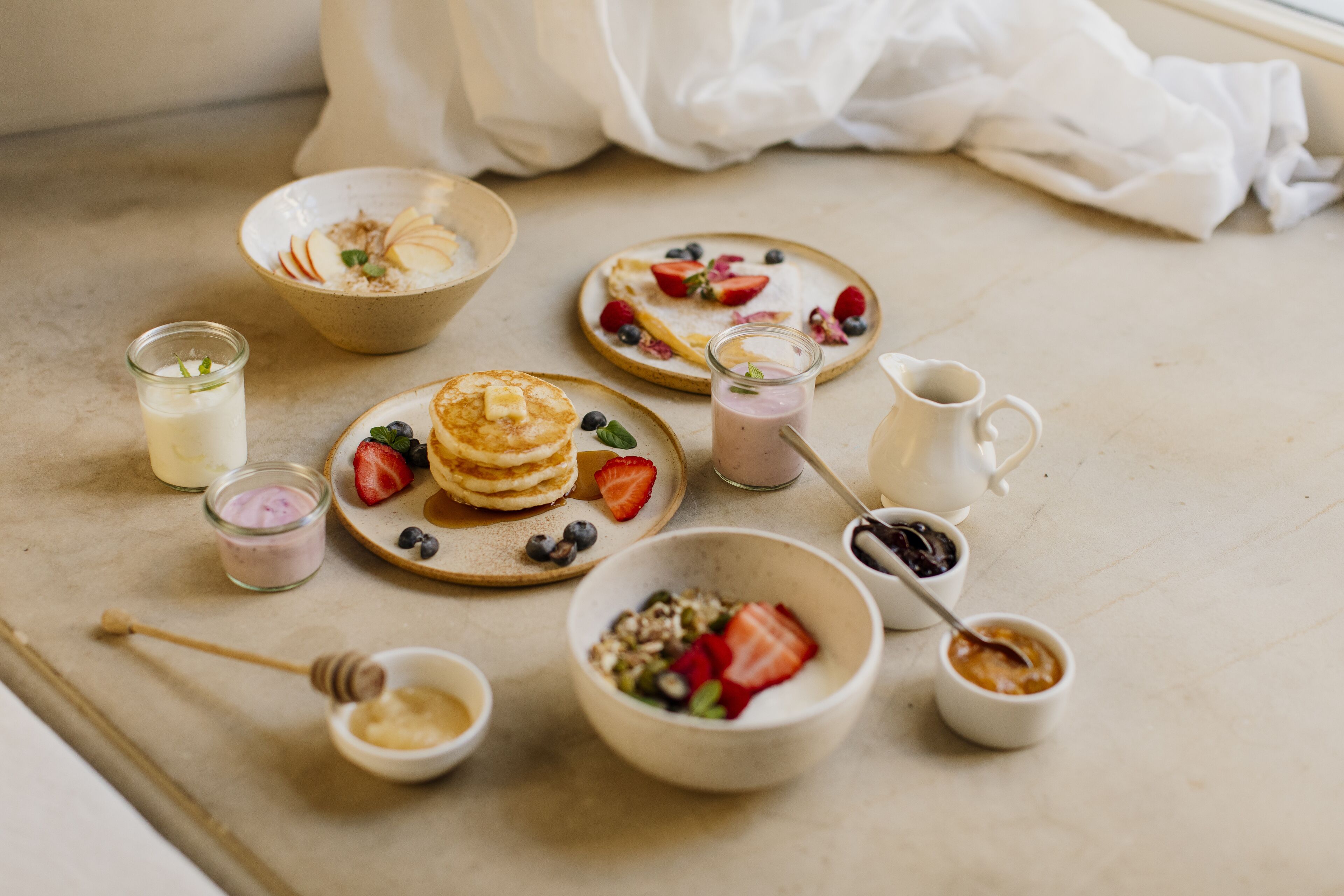 Une table dressée pour le petit-déjeuner, avec des crêpes, des fruits rouges et différentes sortes de confitures.