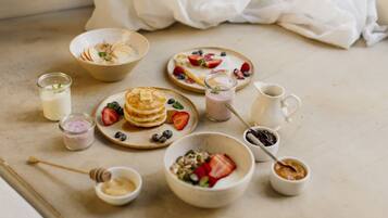 Une table dressée pour le petit-déjeuner, avec des crêpes, des fruits rouges et différentes sortes de confitures.