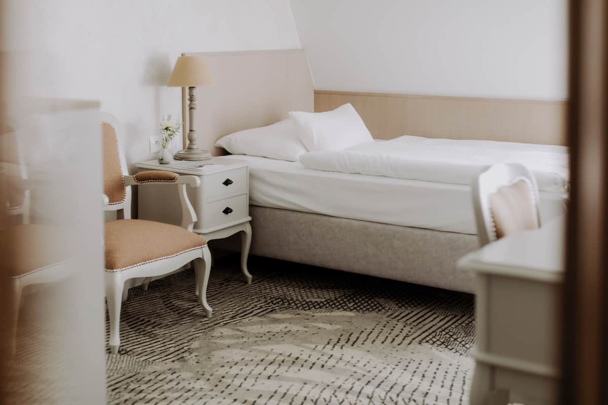 Una habitación de hotel con una cama, una silla, una mesita de noche y una lámpara.