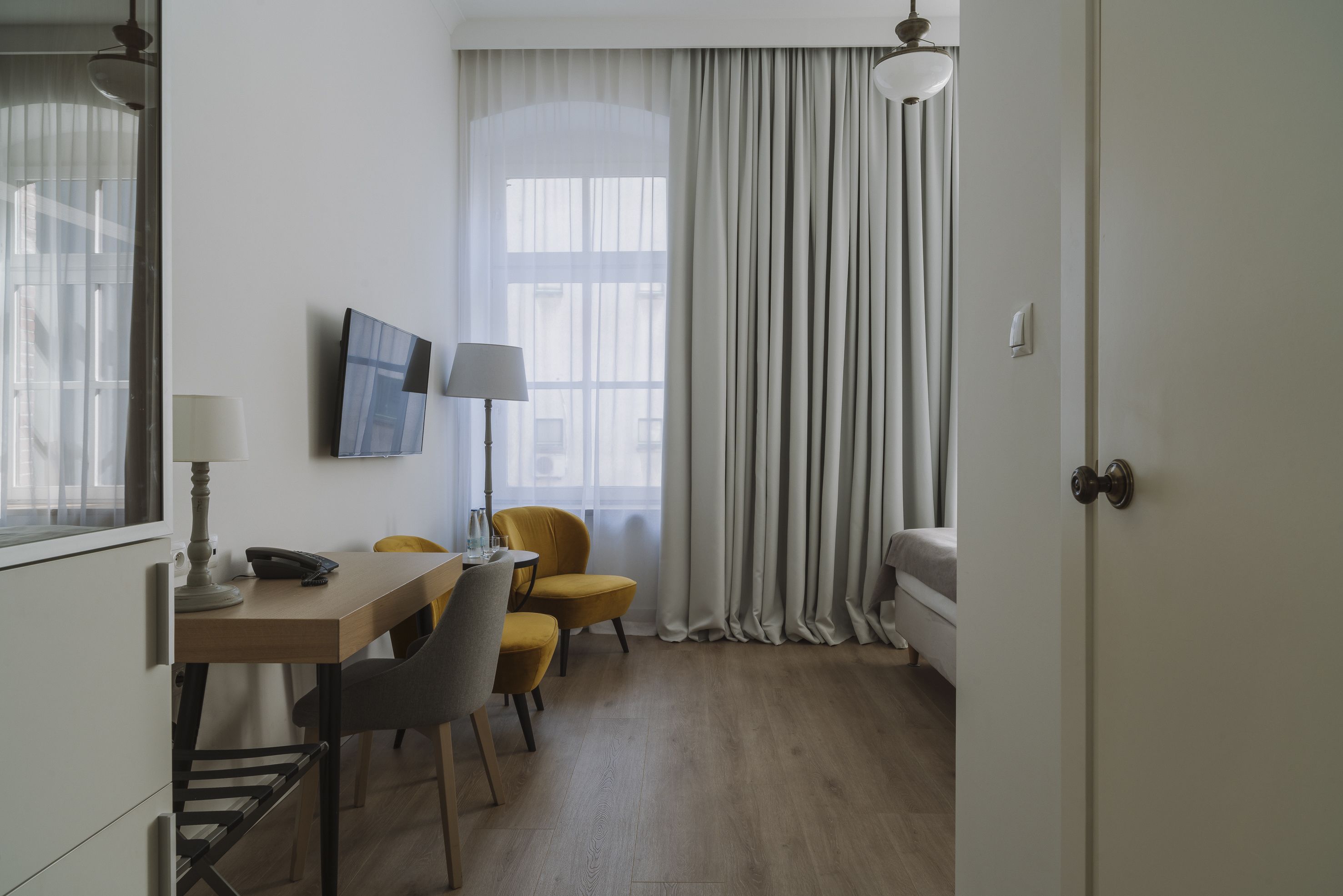 Une chambre d’hôtel avec un bureau en bois, deux chaises, un lit, une télévision et une fenêtre avec des rideaux.