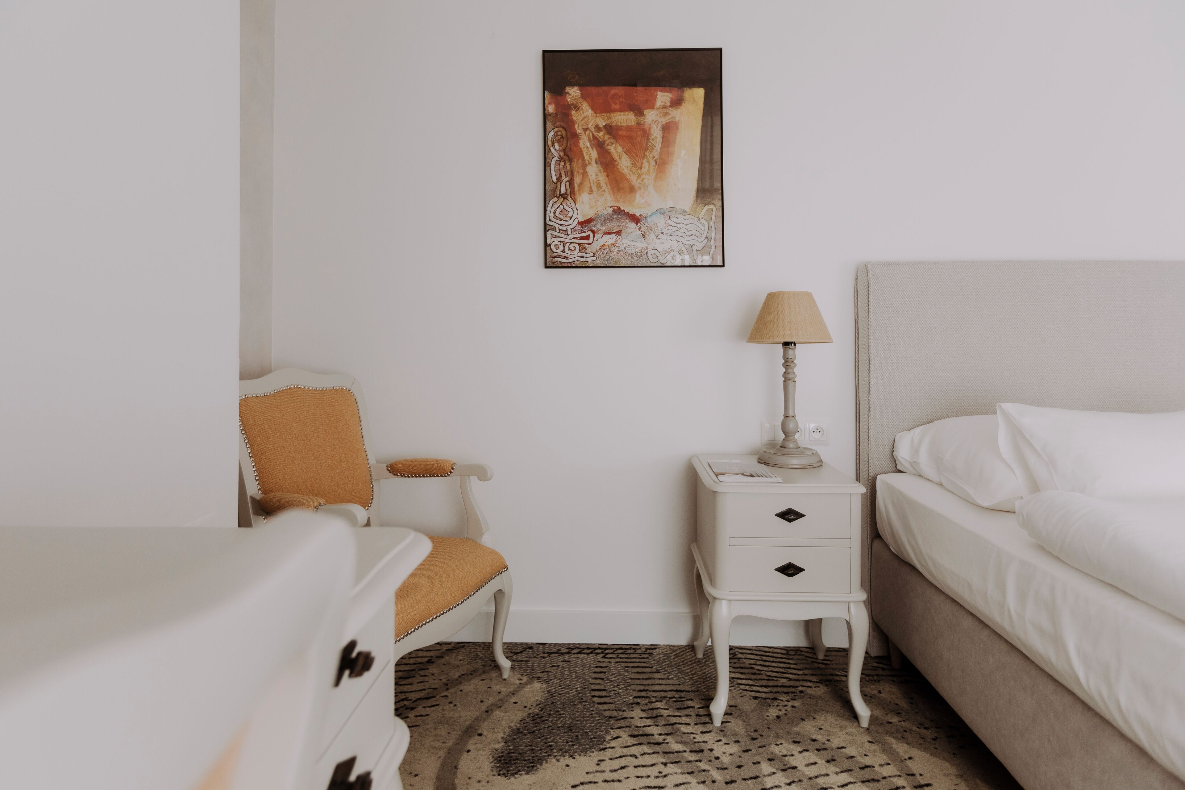Een hotelkamer met een bed, een stoel, een nachtkastje met een lamp en een schilderij aan de muur.
