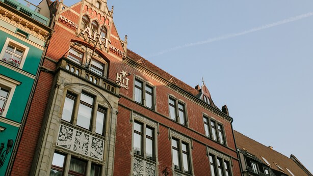 A historic building with a prominent arched entrance, a sign for a hotel and casino, and a clear blue sky in the background. - Art Hotel (Wroclaw)