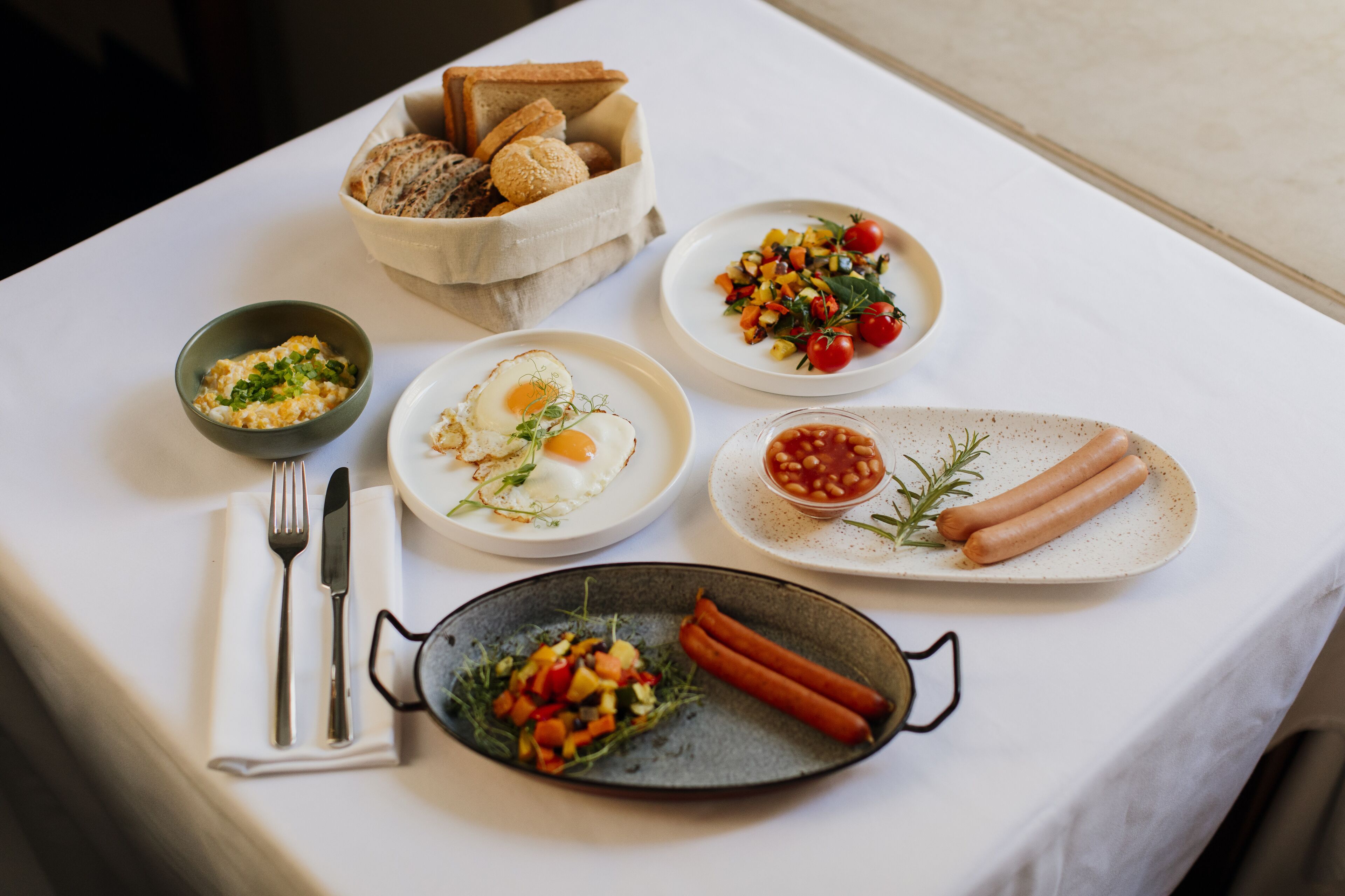 A breakfast table with various dishes including eggs, vegetables, and sausages.