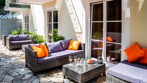 A patio area with wicker furniture, a stone floor, and a glass door leading to a balcony. - Hotel Spitzberg (Passau)