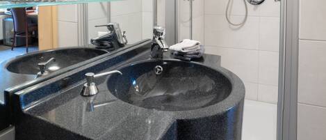 A modern bathroom with a black granite sink, a glass shelf with glasses, and a shower with a handheld showerhead.