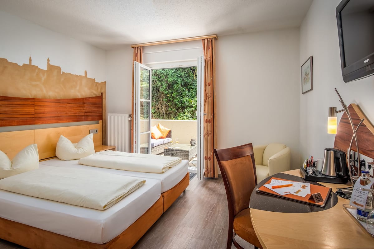 Une chambre d’hôtel avec un grand lit, un bureau avec une chaise, une télévision et une vue sur la verdure par la fenêtre.
