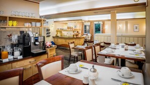 A hotel dining area with wooden tables, chairs, and a coffee station. - Hotel Spitzberg (Passau)