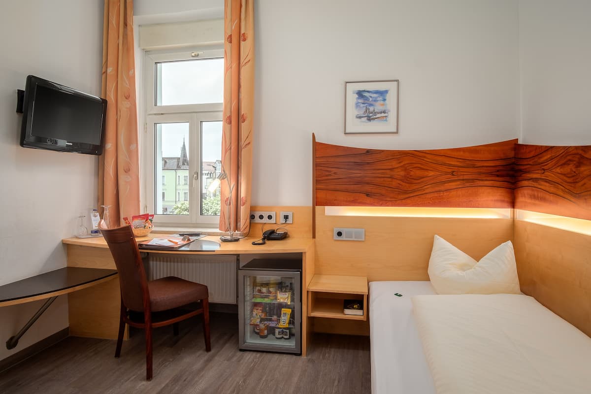Une chambre d’hôtel avec une tête de lit en bois, un bureau avec une chaise, un lit, un téléviseur fixé au mur et une fenêtre avec des rideaux.