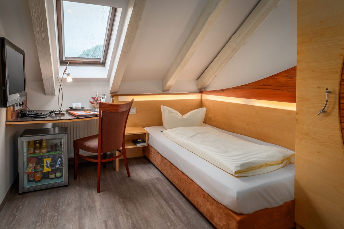 Une chambre de taille réduite comprenant un lit, un bureau, une chaise et un petit réfrigérateur.
