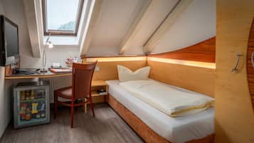 A compact room with a bed, desk, chair, and a small refrigerator.