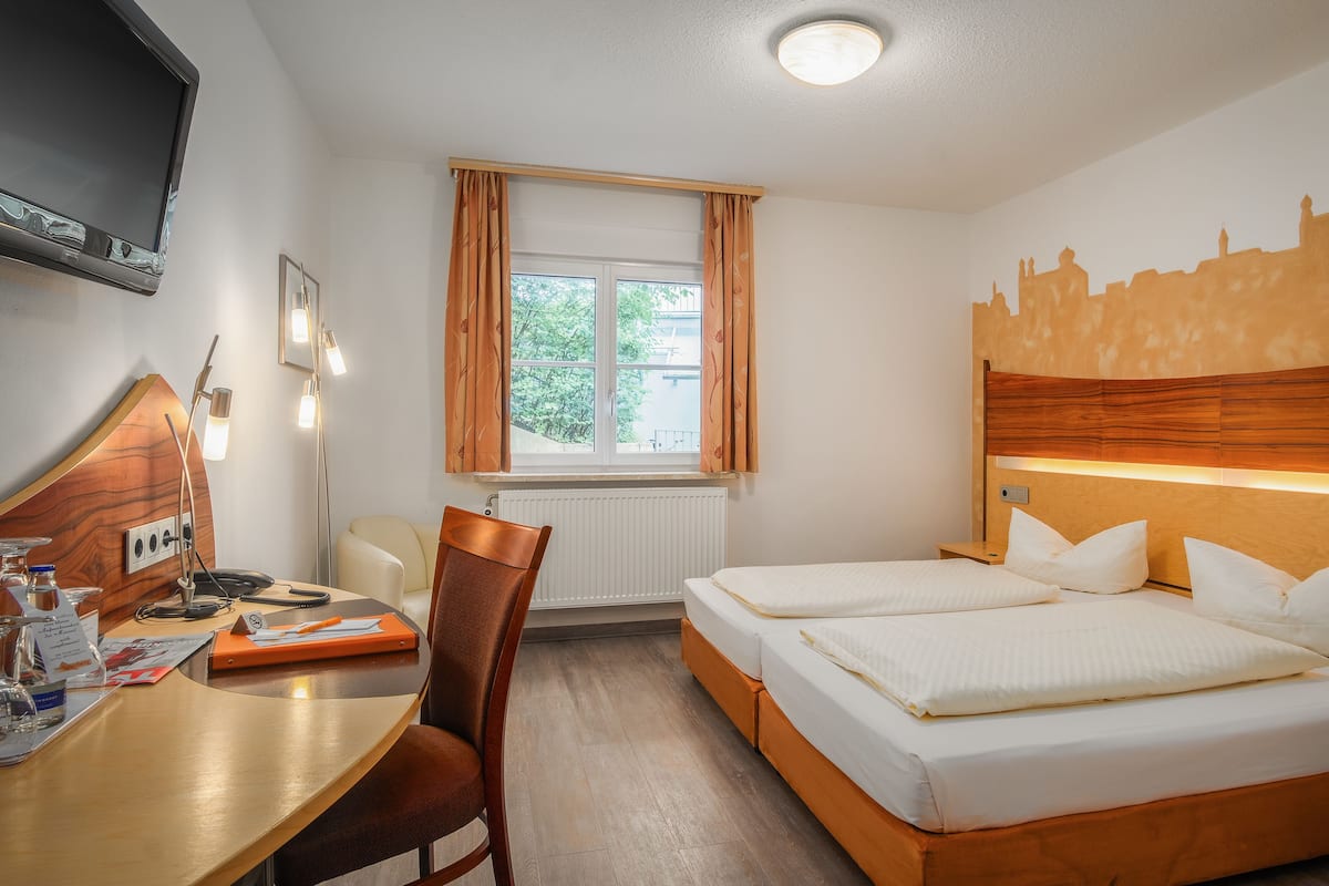 Une chambre d’hôtel avec un lit, un bureau, une chaise, une télévision et une fenêtre avec des rideaux.