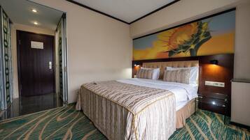 A hotel room with a large bed, a headboard with a floral mural, a glass side table, and a carpeted floor.