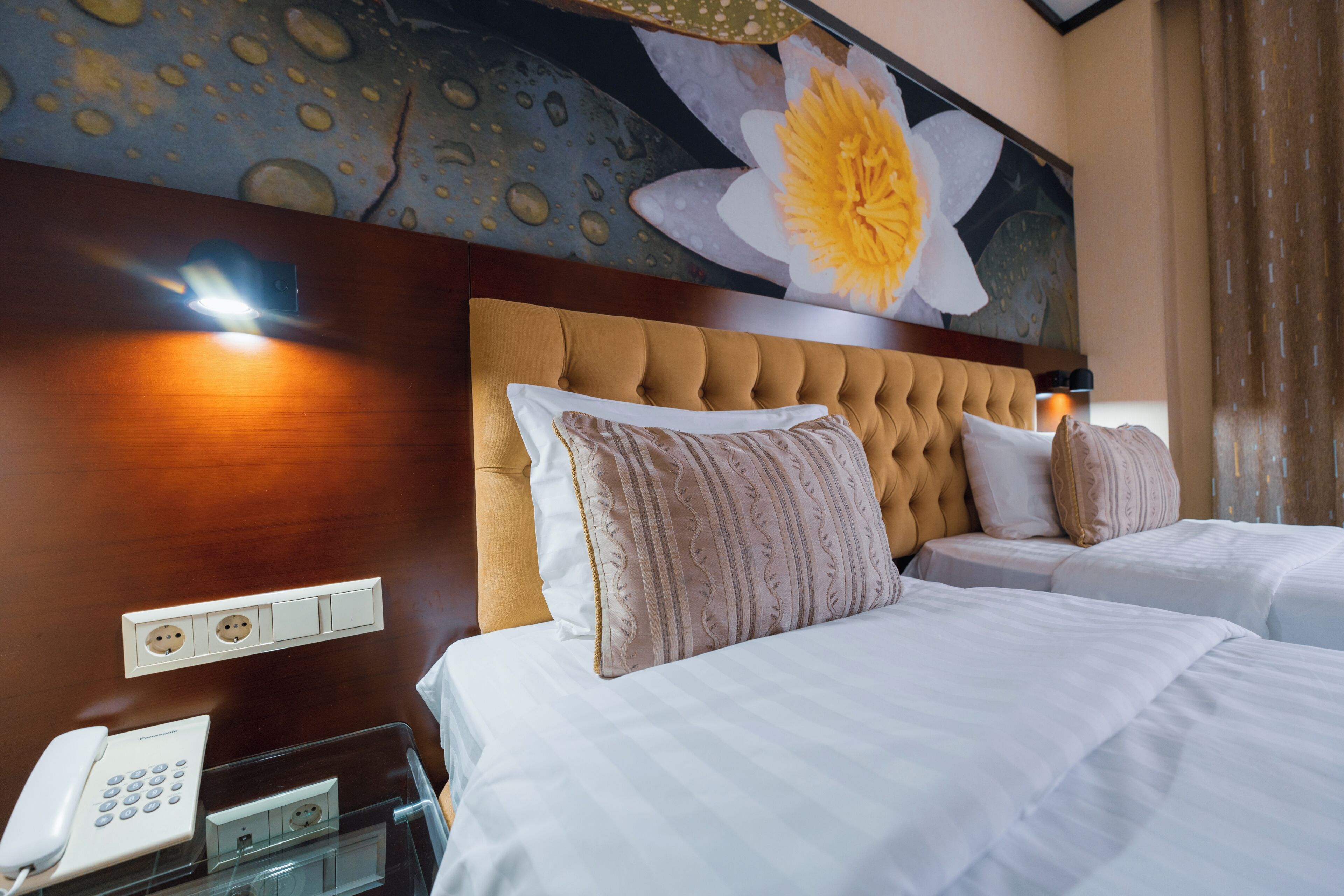 Ein Hotelzimmer mit geblattetem Kopfteil, zwei Betten, einem Telefon und einer Wandleuchte.