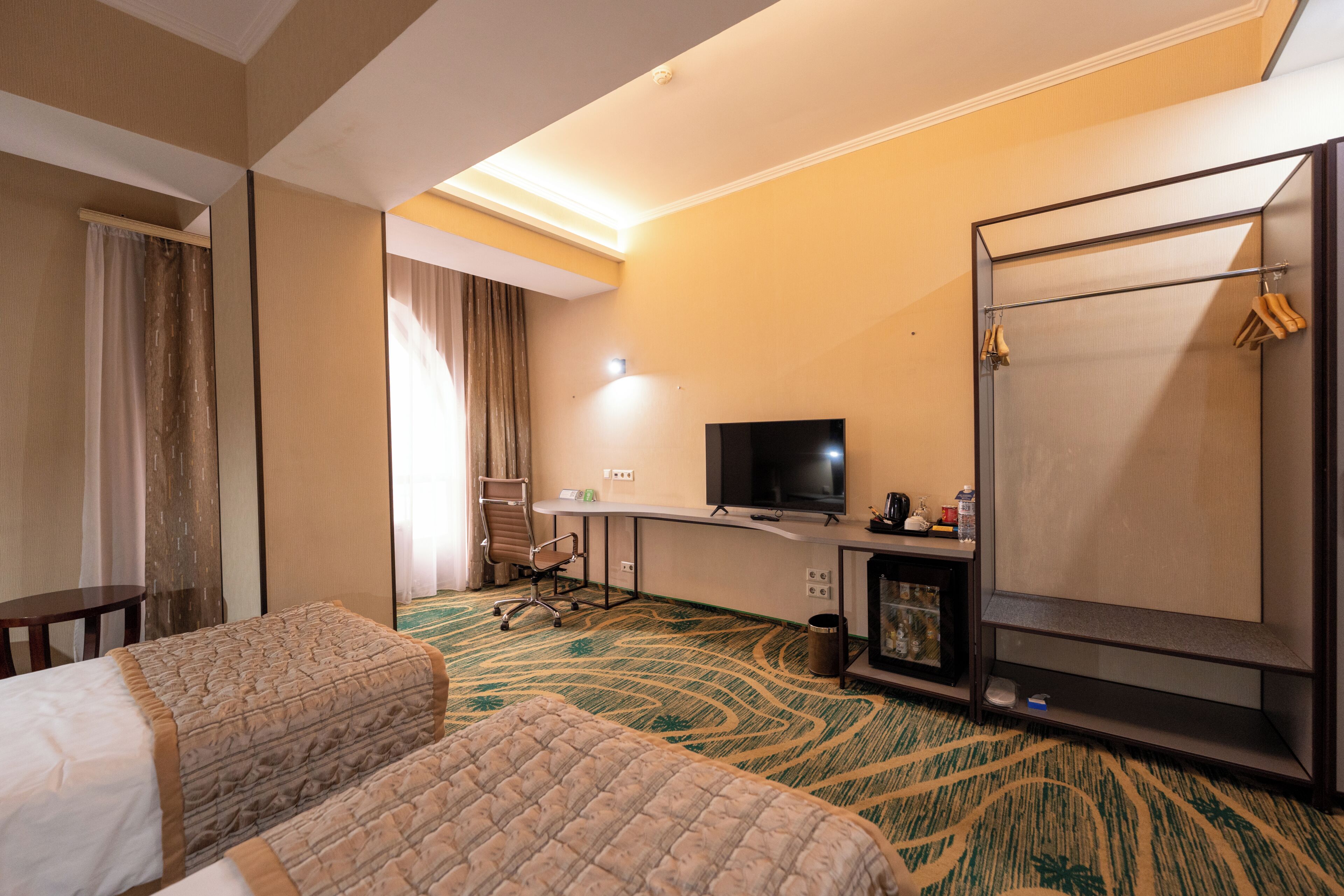 Quarto de hotel com cama, escrivaninha com televisão, cadeira e chuveiro.