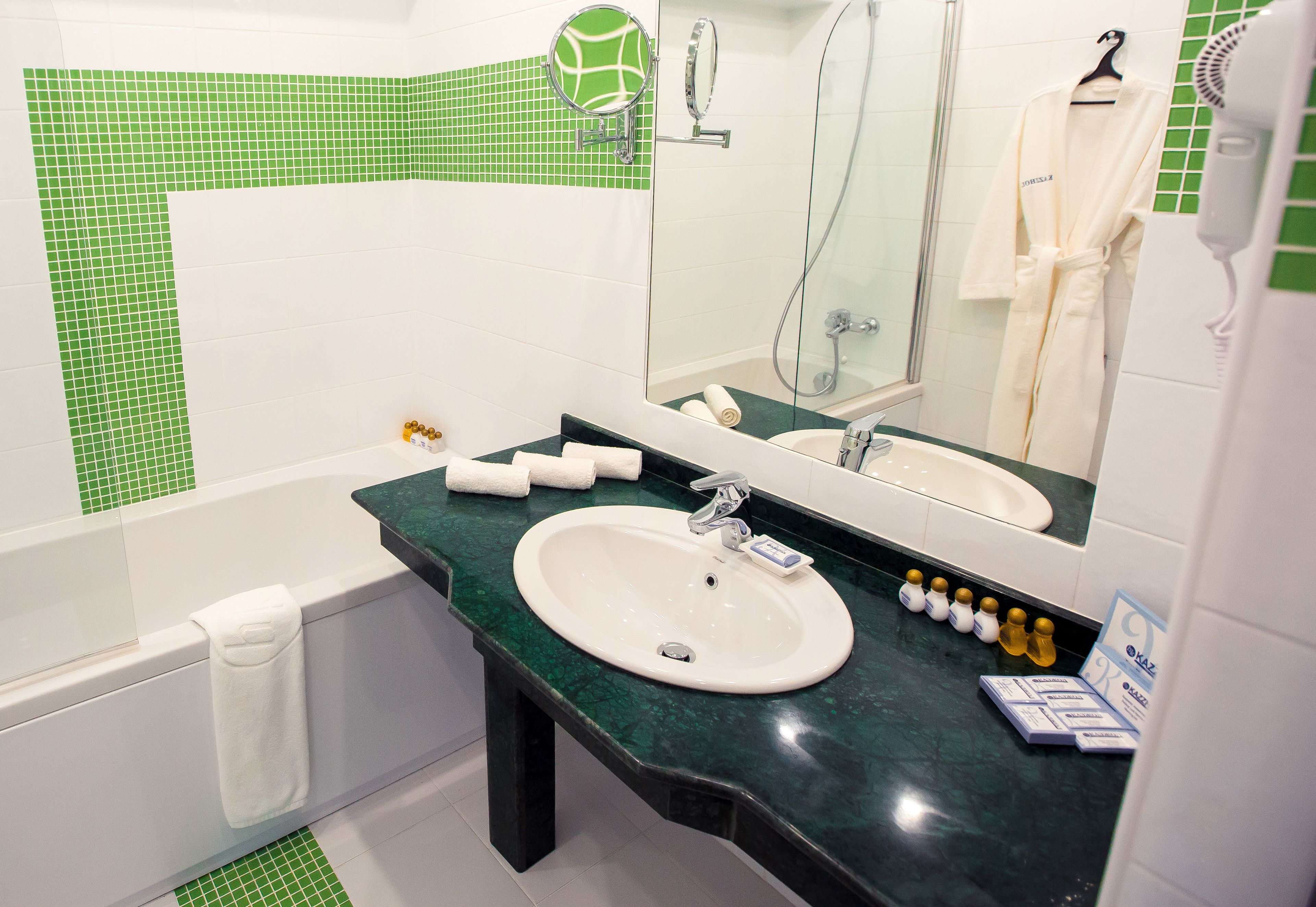 A bathroom with a green and white tiled wall, a white sink, a mirror, a towel rack, and a hairdryer.