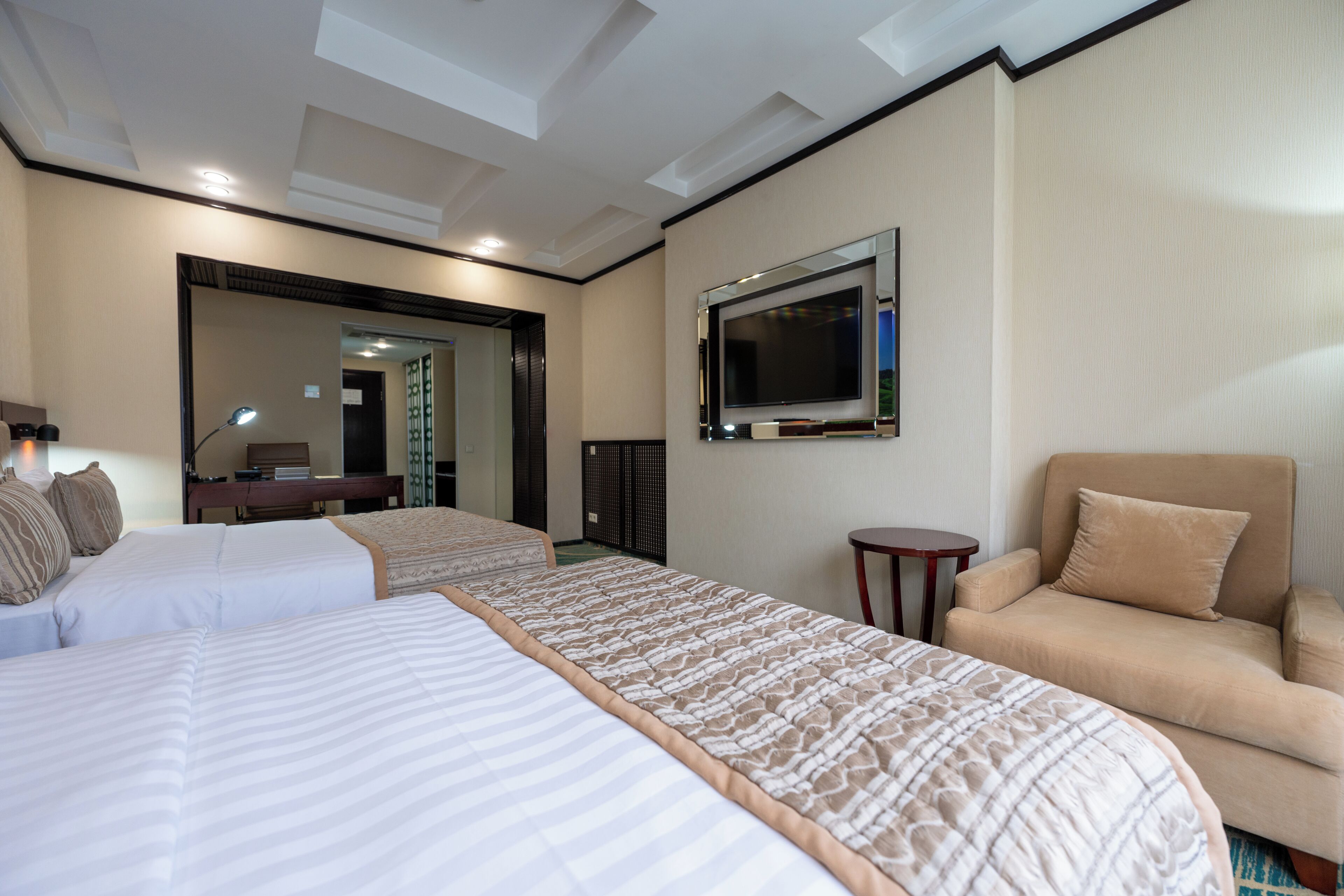 A hotel room with two beds, a sofa, a TV, and a desk with a lamp.
