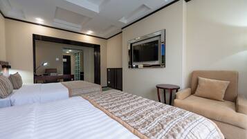 A hotel room with two beds, a sofa, a TV, and a desk with a lamp.