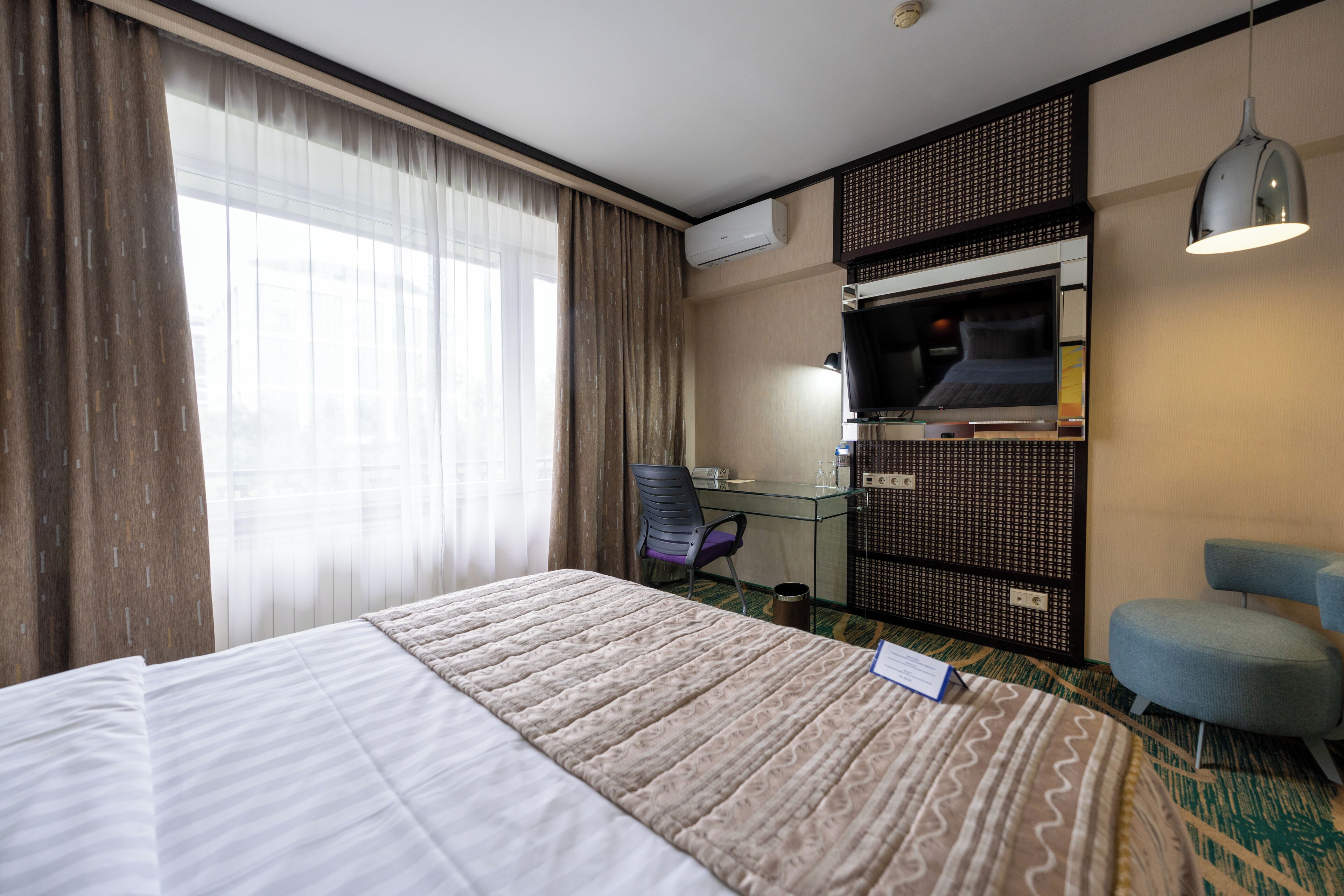 Una habitación de hotel con una cama grande, un escritorio con computadora, una silla y un televisor.