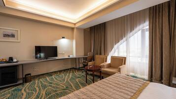 A hotel room with a large bed, a desk with a flat-screen TV, a chair, and a small table.