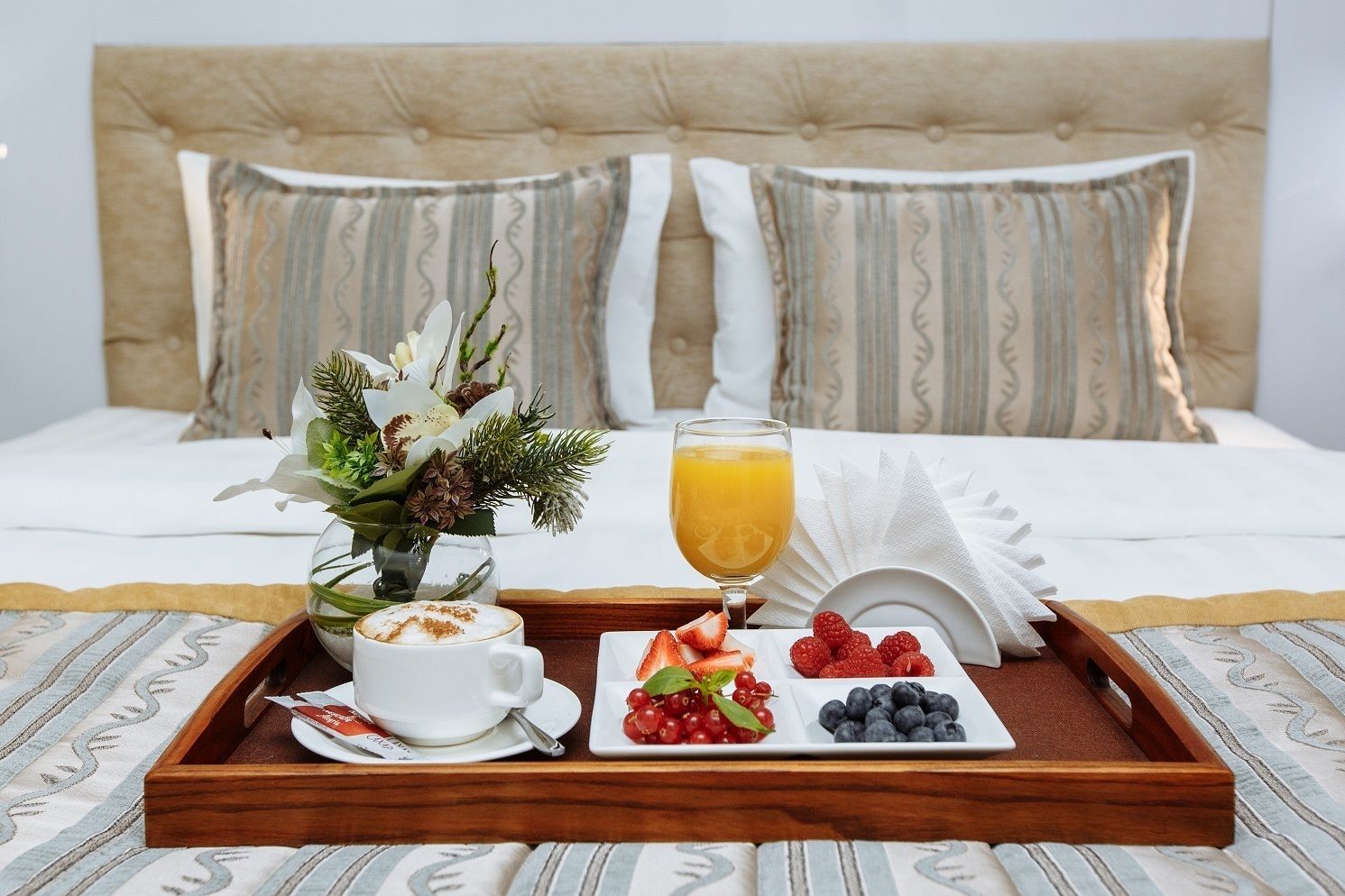 Bandeja de desayuno con café, fruta y jugo sobre una cama con almohadillas a rayas.
