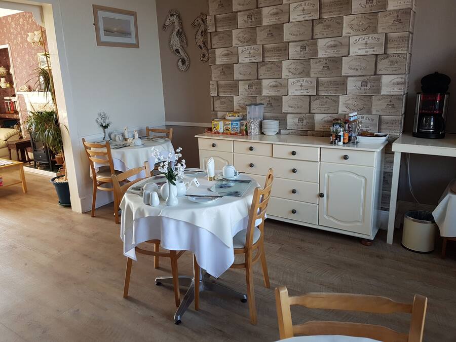 A dining area with a white table set for four, wooden chairs, and a wall decorated with vintage wine boxes.
