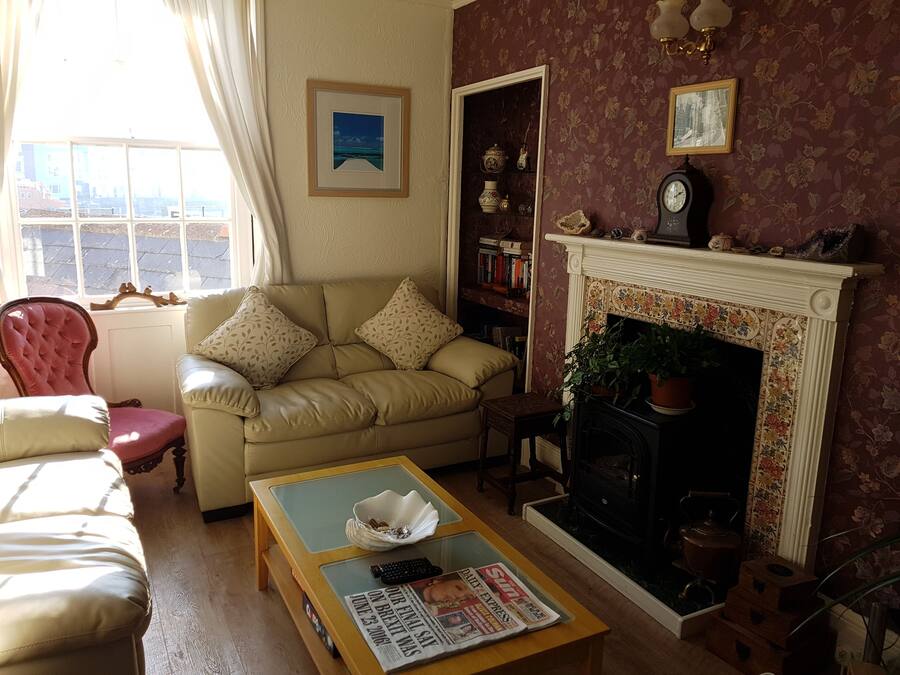 A living room with a beige sofa, a red armchair, a fireplace, a bookshelf, and a window with curtains.