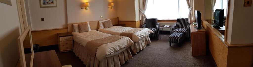 A hotel room with two beds, a desk, a chair, and a TV.