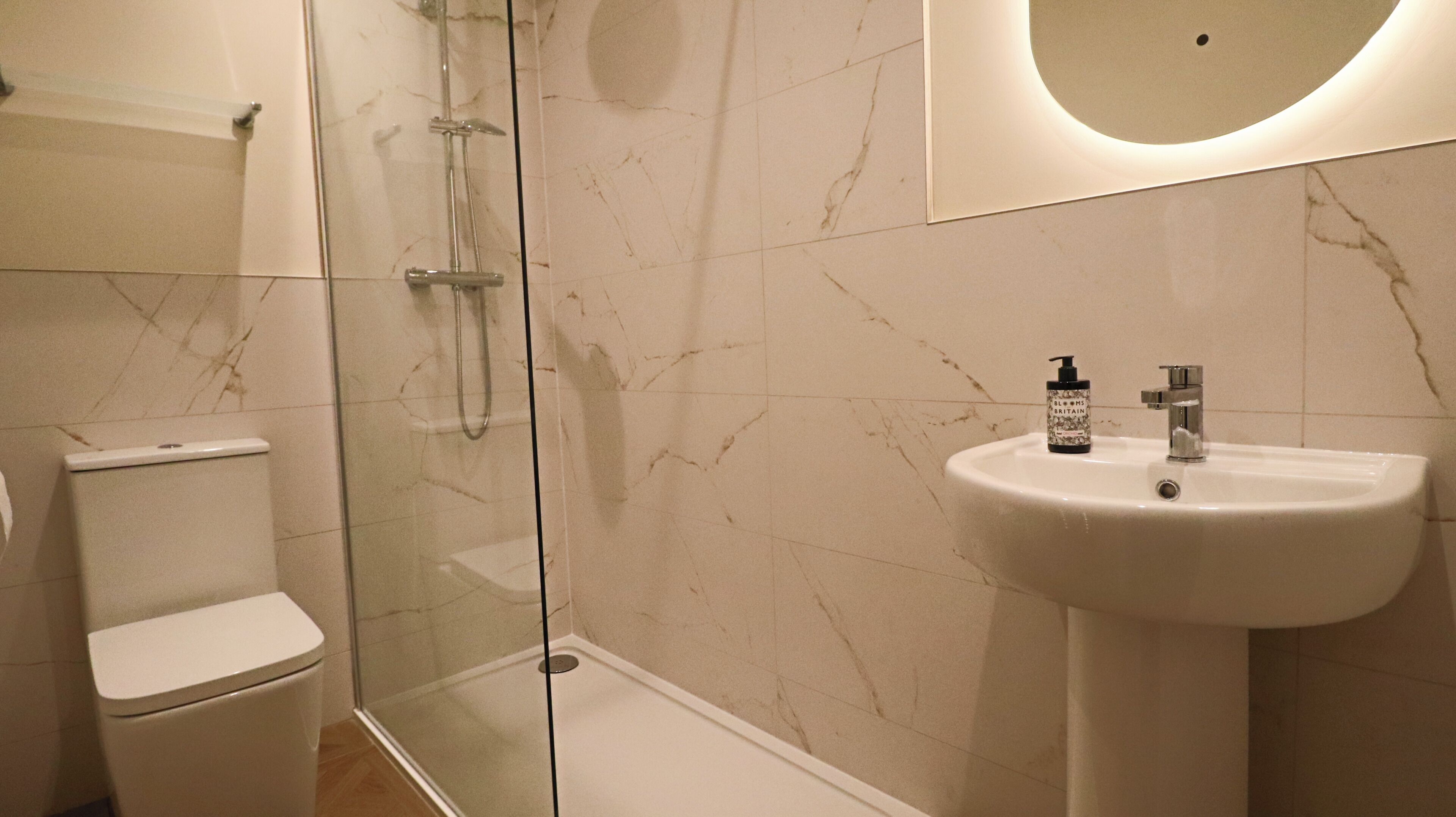 A bathroom with a toilet, a glass-enclosed shower, and a sink with a bottle of hand soap.