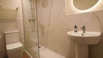 A bathroom with a toilet, a glass-enclosed shower, and a sink with a bottle of hand soap.