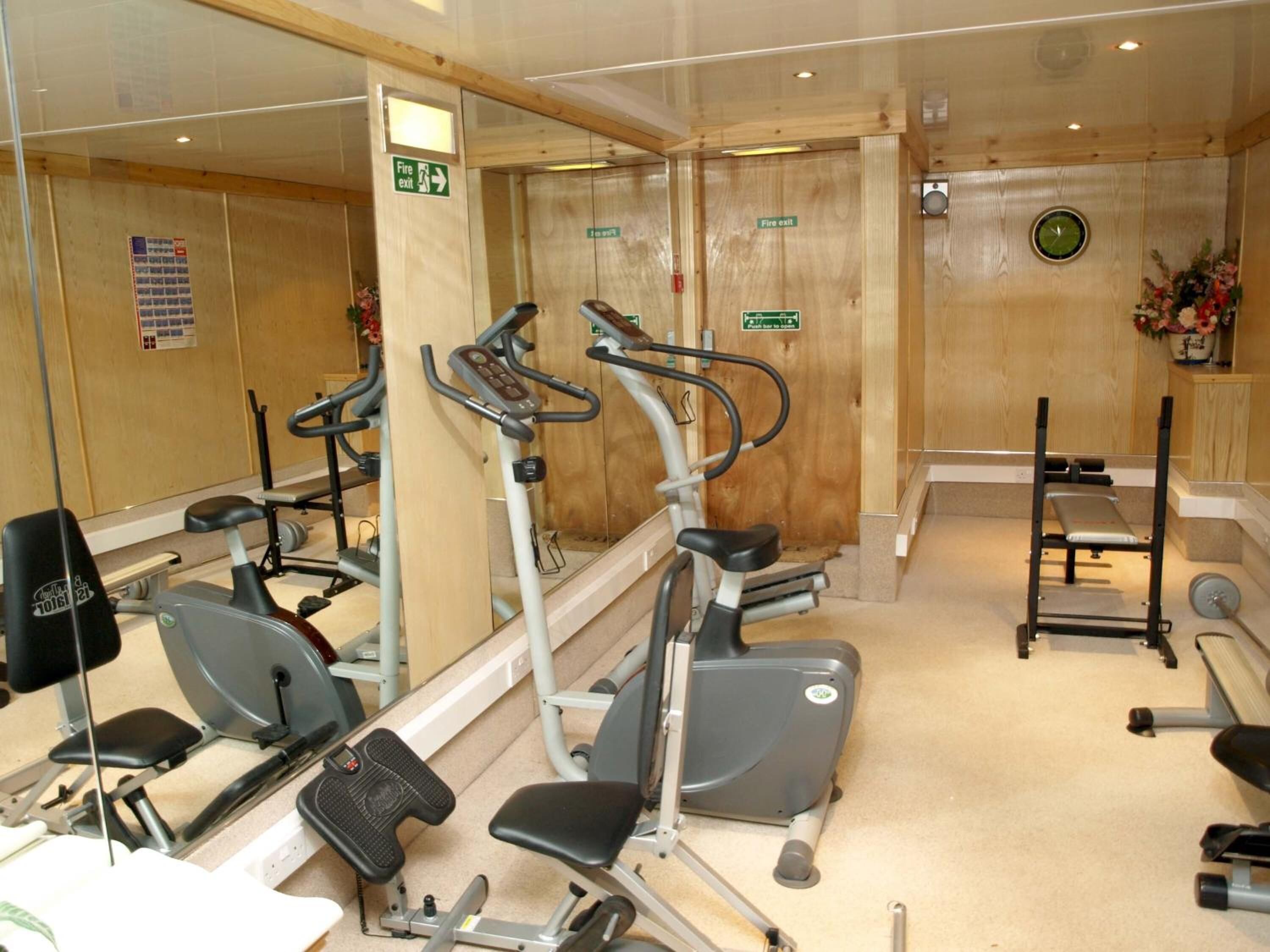Une salle de sport équipée de machines de cardio, d’un banc de développé couché et d’un miroir.