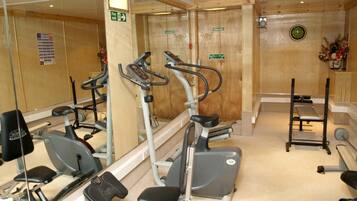 Une salle de sport équipée de machines de cardio, d’un banc de développé couché et d’un miroir.