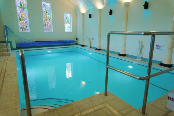 An indoor swimming pool with clear water, a blue mat at the shallow end, and a statue on the wall.