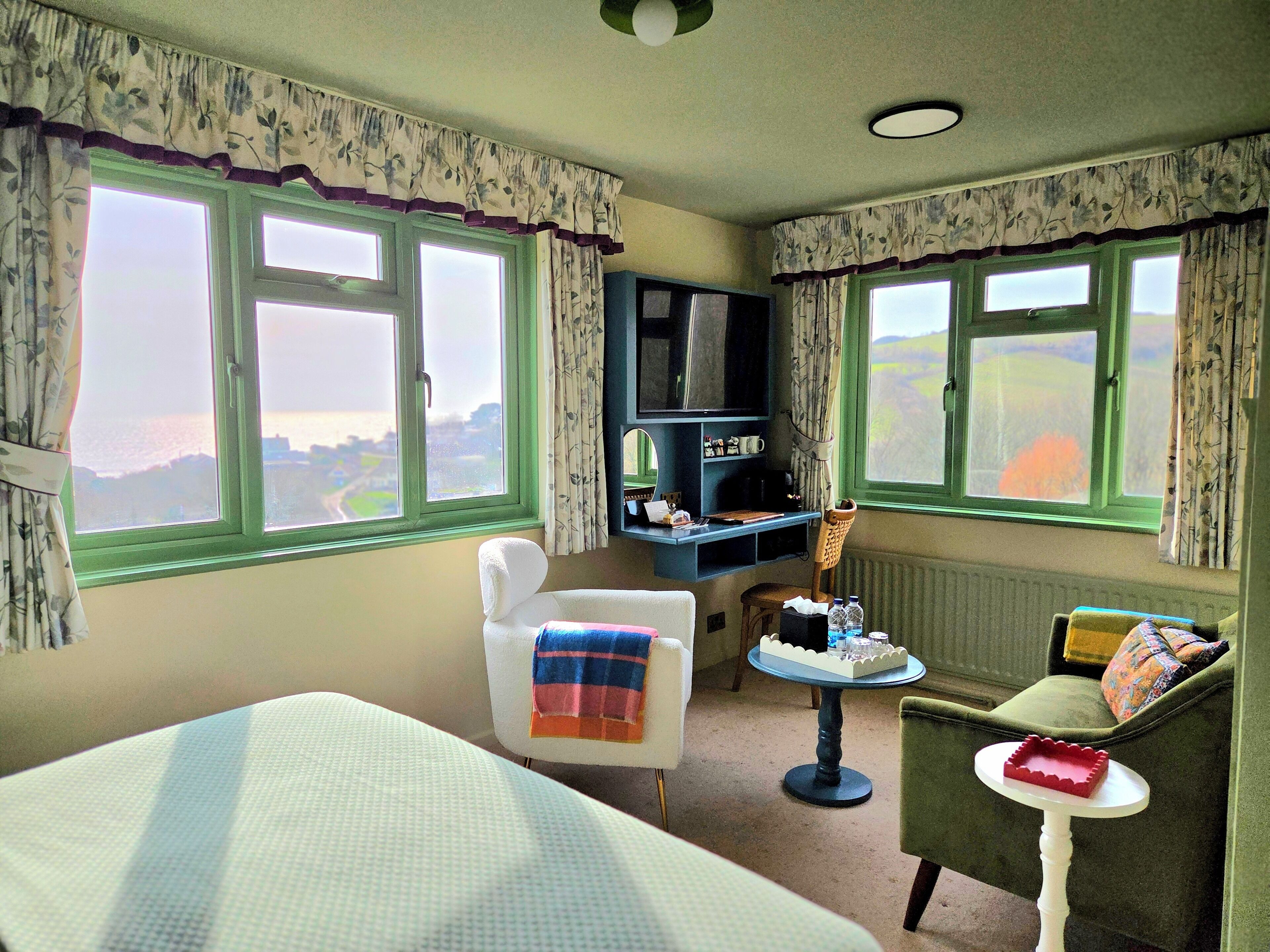 Une chambre comprenant un lit, une chaise, une petite table avec un plateau, un téléviseur et une vue sur l’extérieur grâce à de grandes fenêtres.