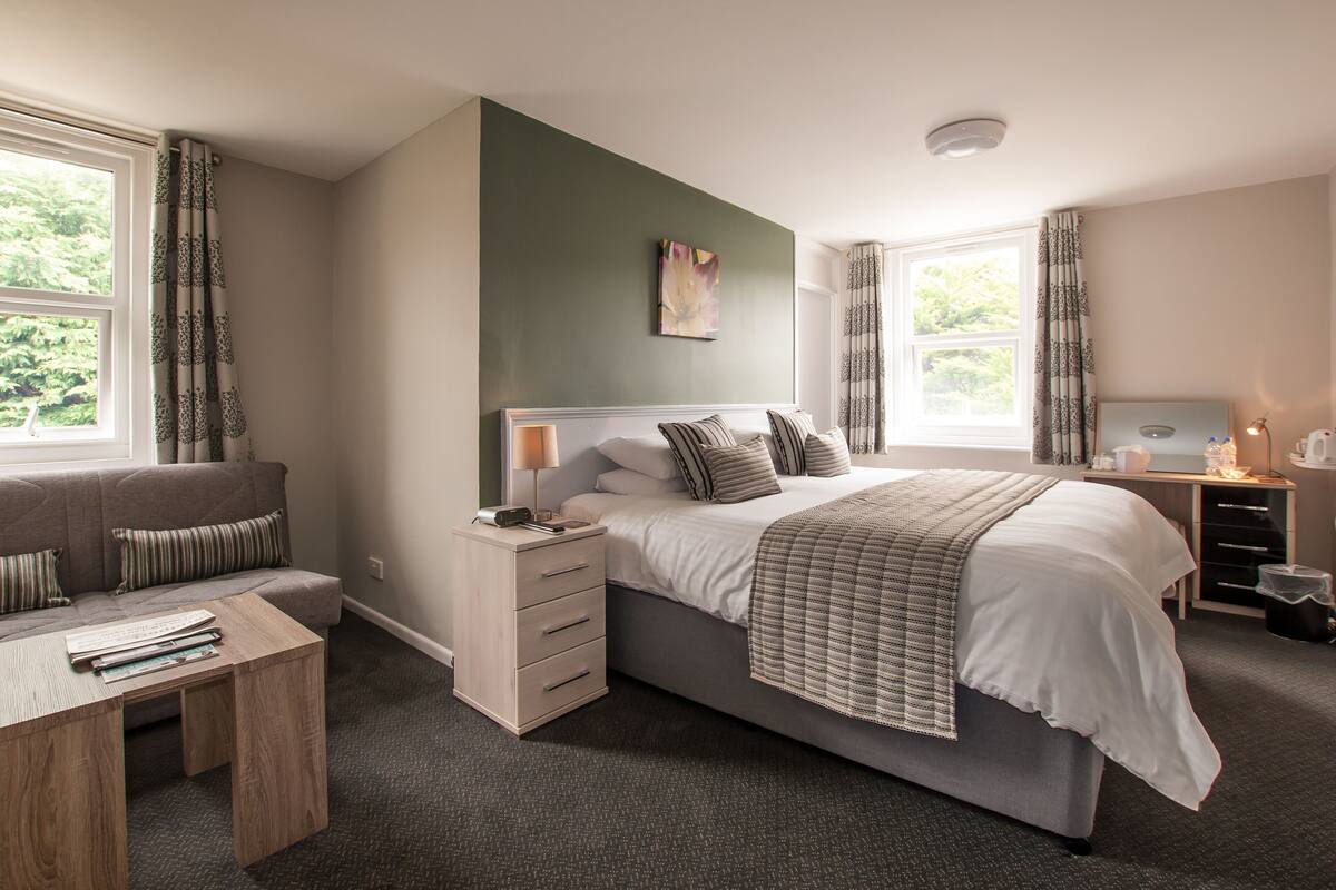 A bedroom with a bed, bedside table, lamp, and a desk with a chair.