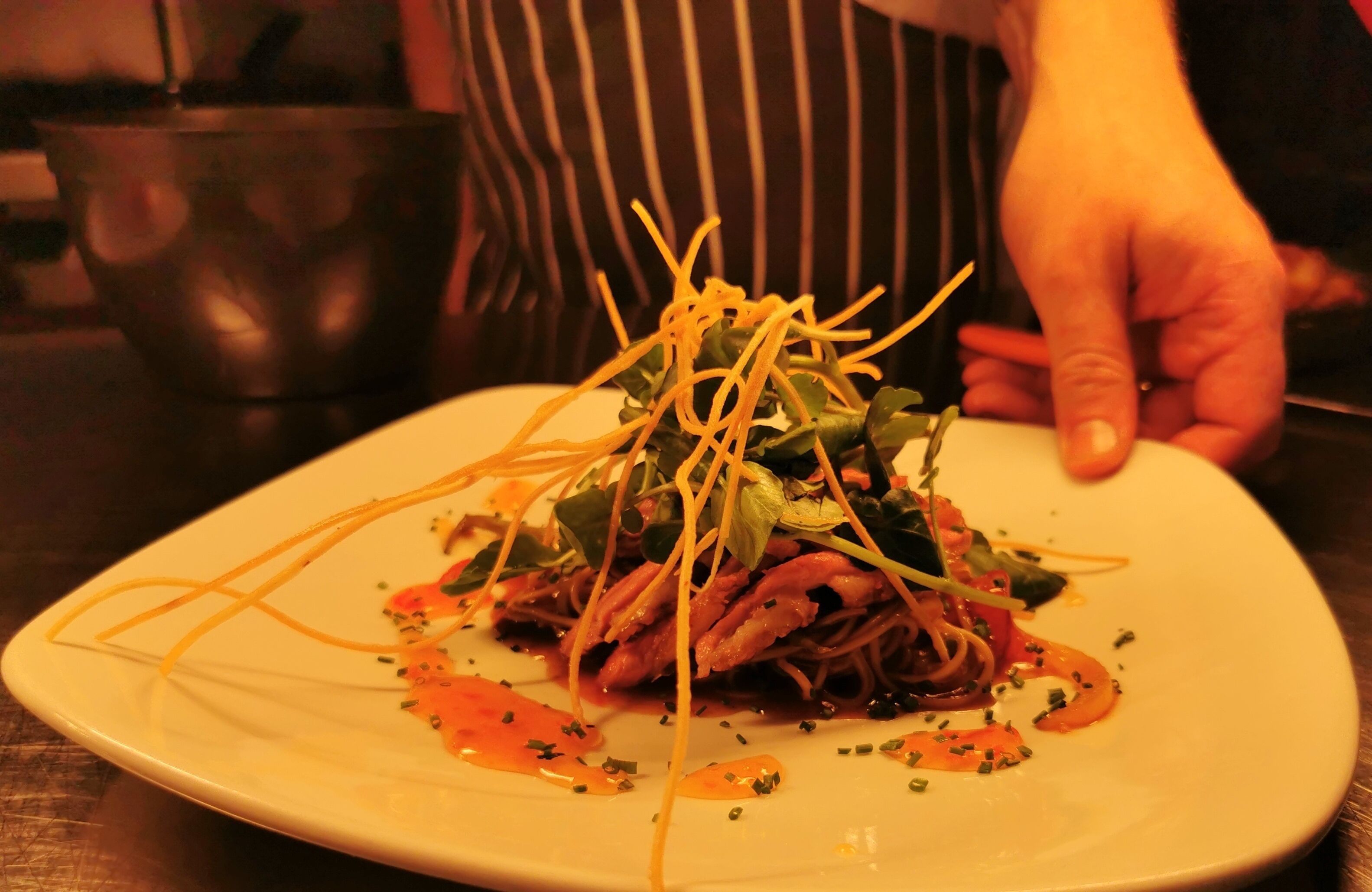 A plate of food with a hand adjusting the garnish.