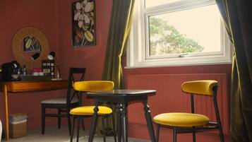 A room with a desk, two yellow chairs, a small table, and a window with curtains.