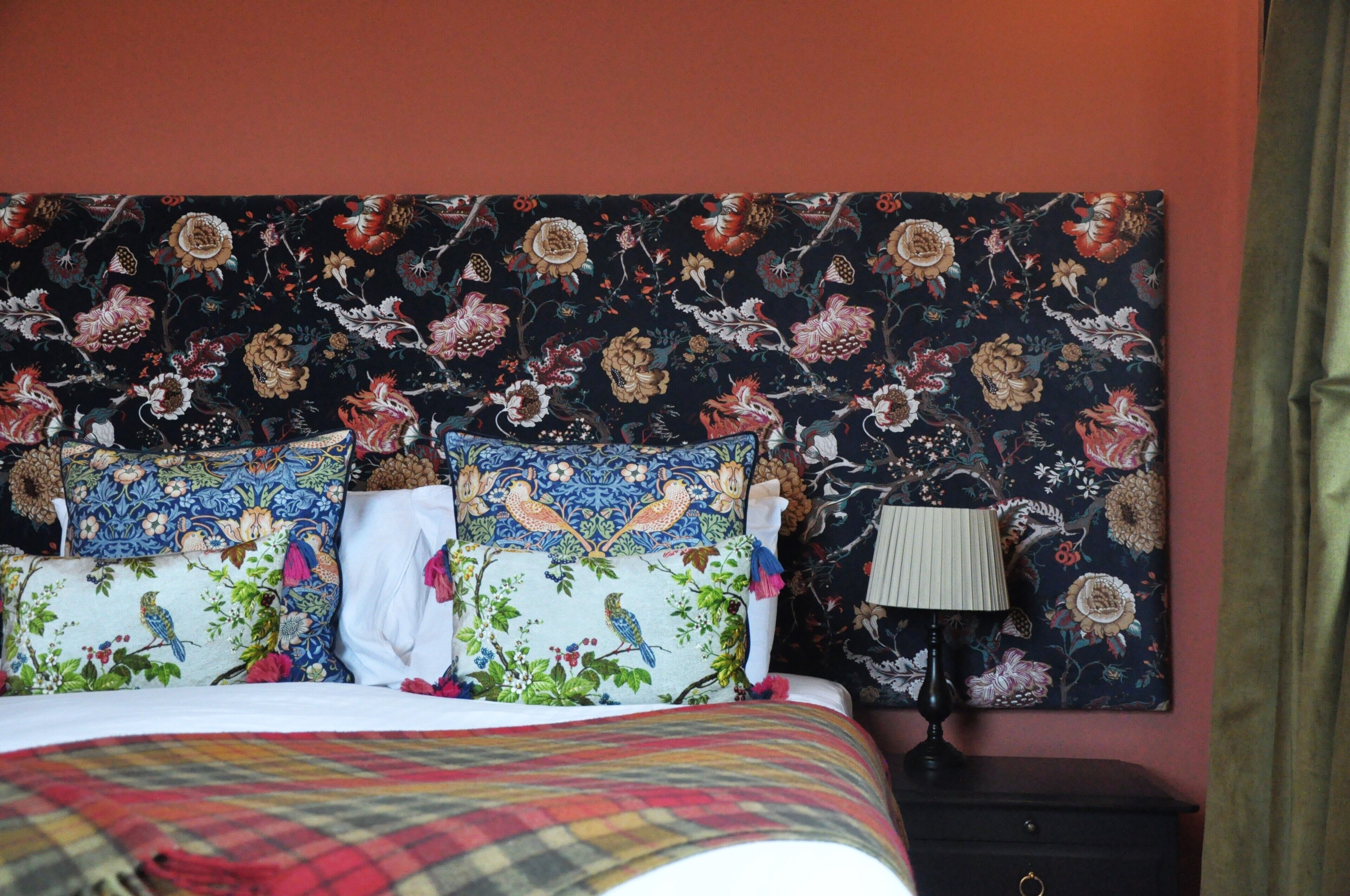 A bed with floral-patterned pillows, a dark headboard, and a nightstand with a lamp.