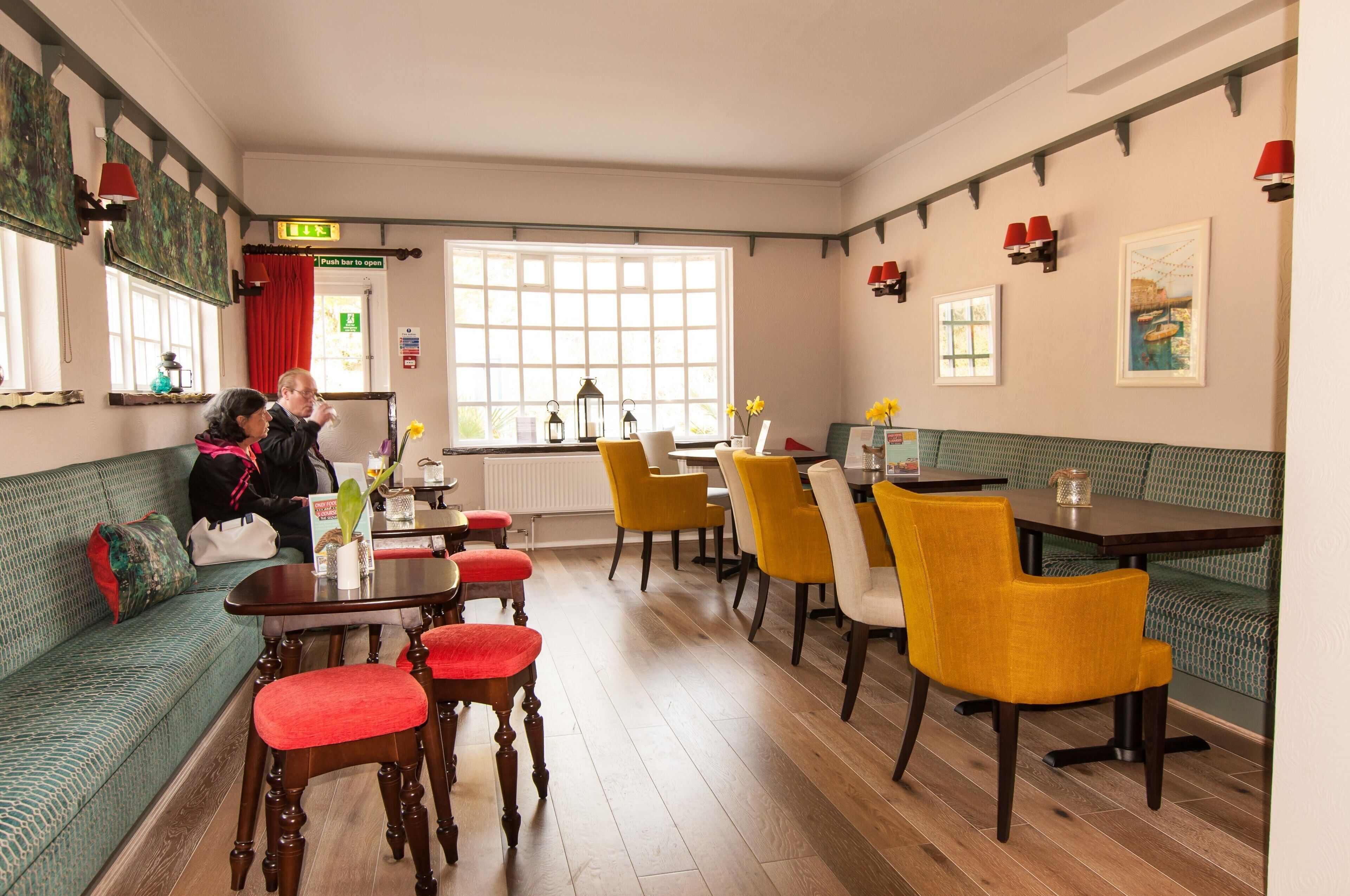 A cozy restaurant with a green sofa, yellow chairs, and wooden tables.