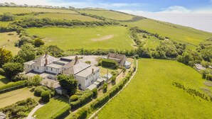 A large white house with multiple rooms, surrounded by green fields and a hilly landscape. - Eype's Mouth Country Hotel (Bridport)